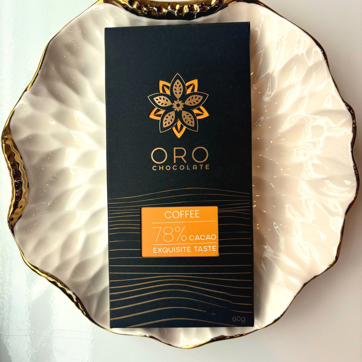 Oro Coffee 78% cacao bar in black packaging on a gold-rimmed white porcelain plate, seen from above