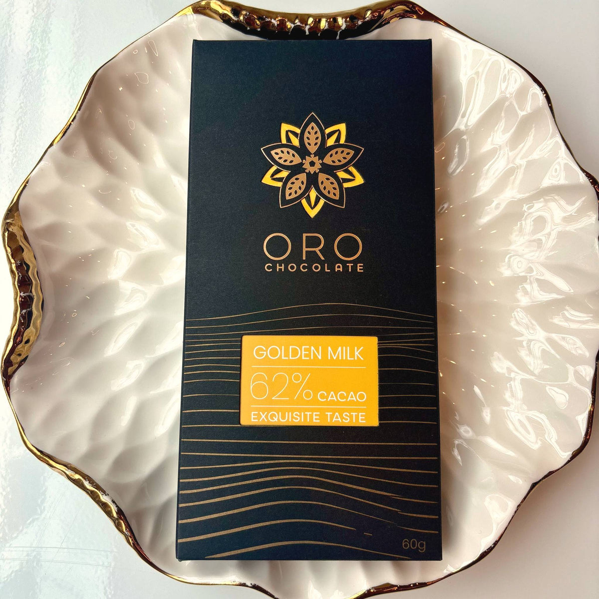 Oro Golden Milk 62% cacao bar in black packaging on a gold-rimmed white porcelain plate, seen from above