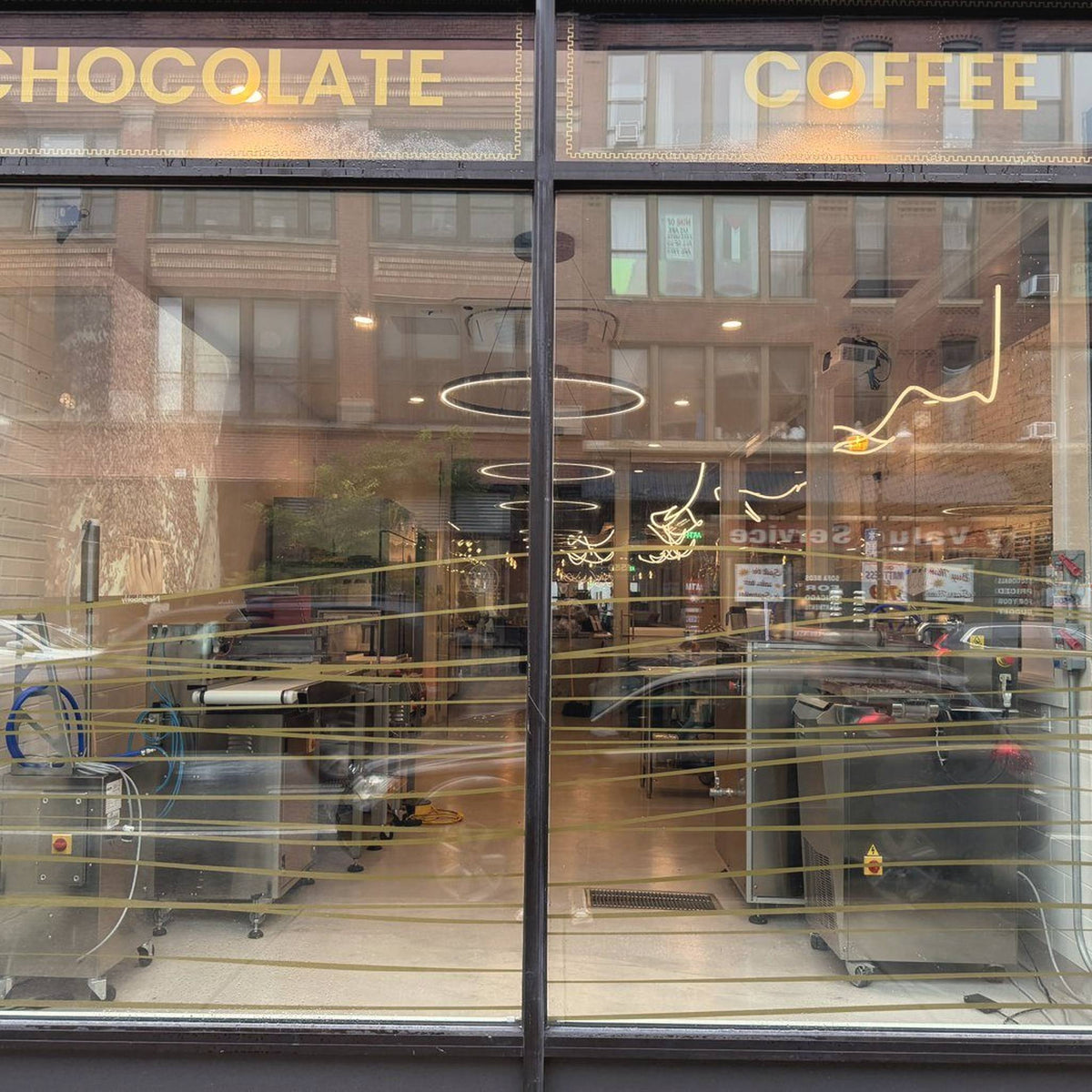 The front window of Oro on Milwaukee Avenue, gold letters reading Chocolate and Coffee, the chocolate equipment behind the glass