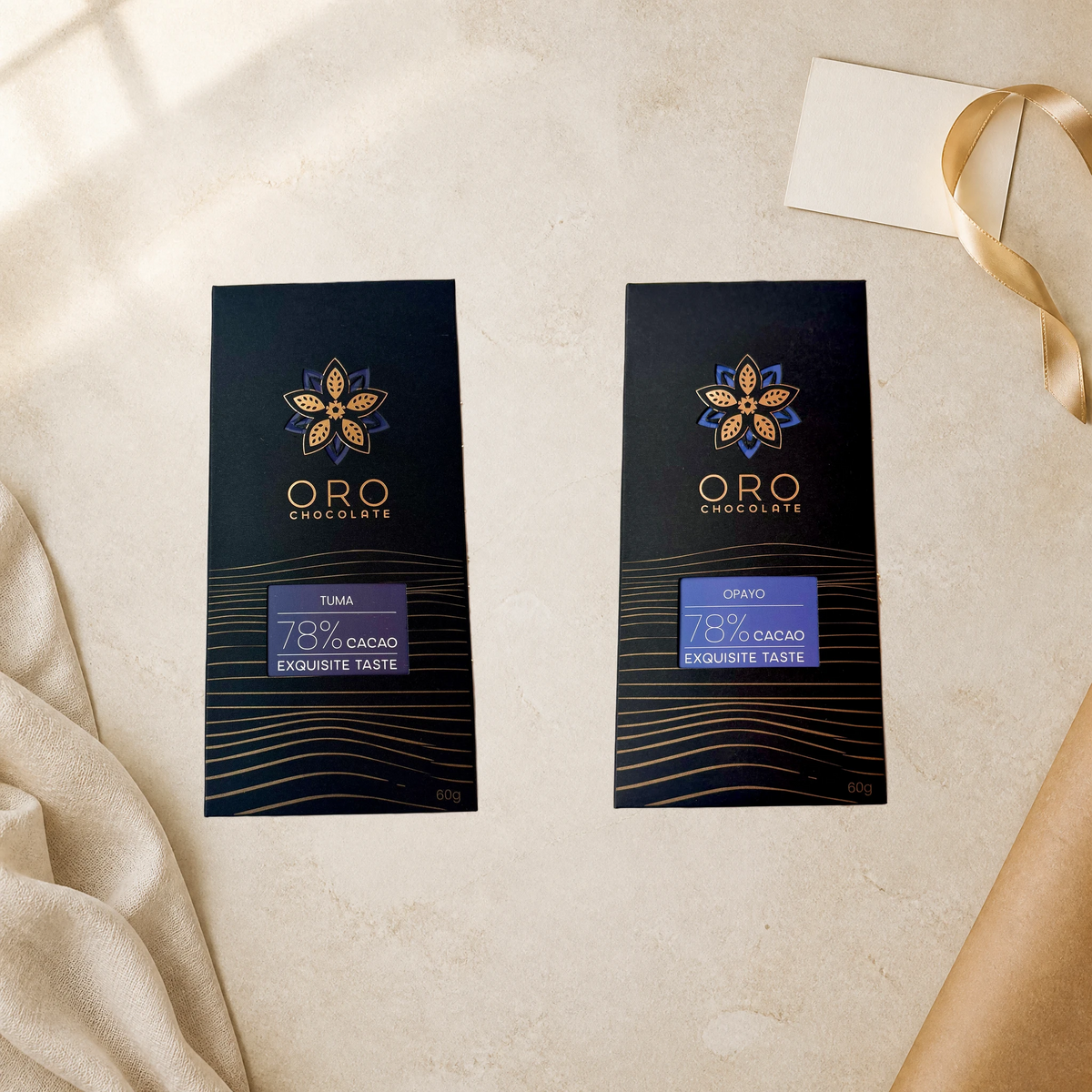 Oro Flight editorial gift setting: Tuma and Opayo 78% cacao bars, 60g each, beside cream linen, a blank note card and gold ribbon.