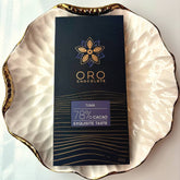 Oro Tuma 78% cacao bar in black packaging on a gold-rimmed white porcelain plate, seen from above