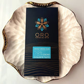 Oro Single Origin Dark 78% cacao bar in black packaging on a gold-rimmed white porcelain plate, seen from above