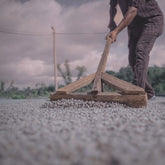 A man pushing a wooden rake through coffee drying on a wide patio, Nicaragua