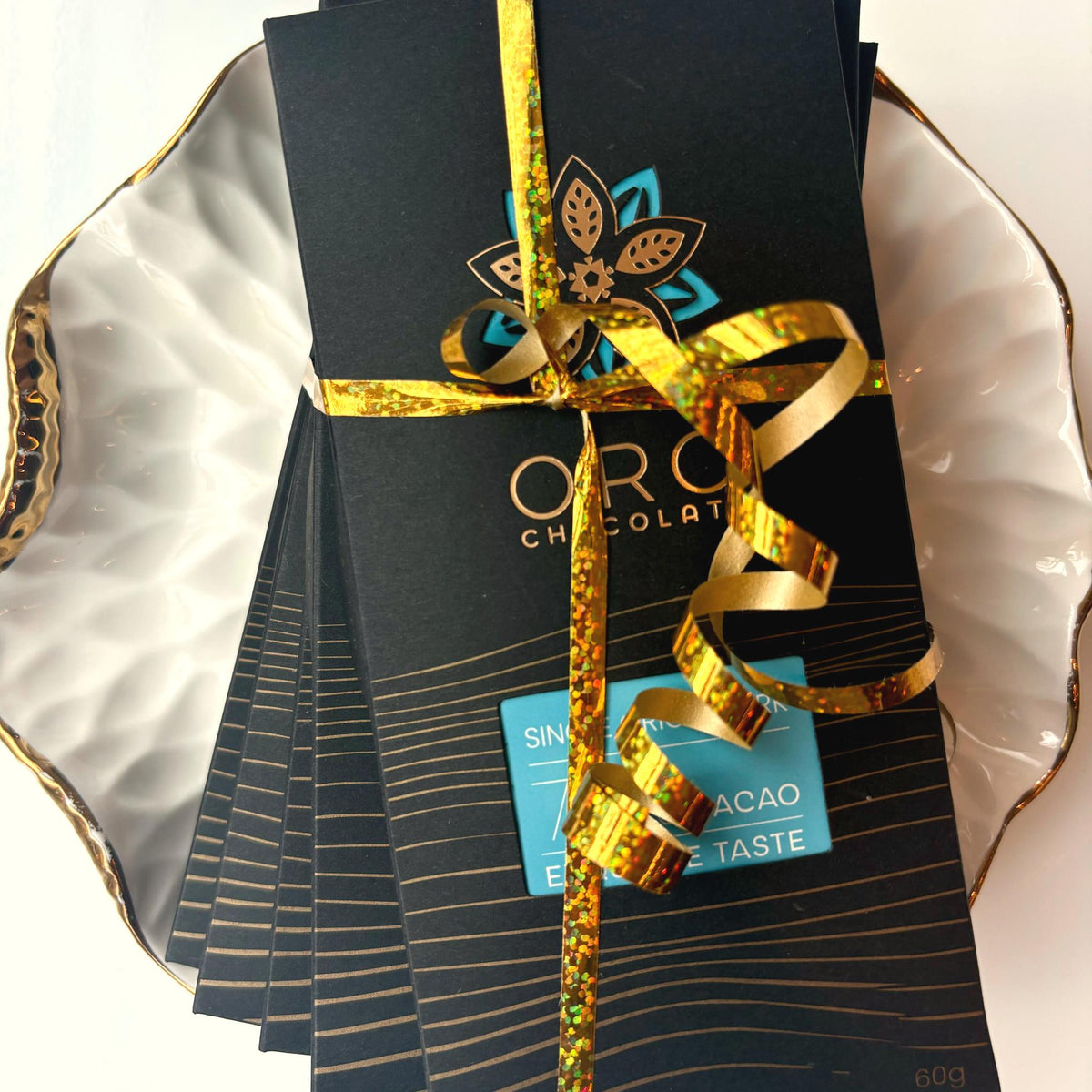 A stack of Oro bars in black packaging tied with a gold ribbon on a gold-rimmed white porcelain plate, seen from above