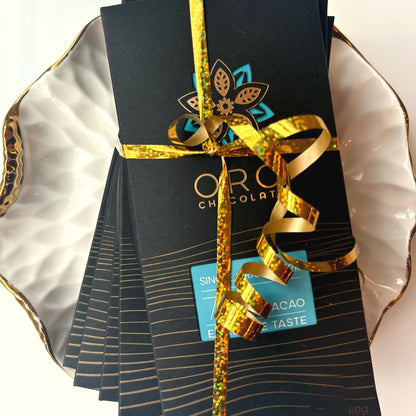 A stack of Oro bars in black packaging tied with a gold ribbon on a gold-rimmed white porcelain plate, seen from above