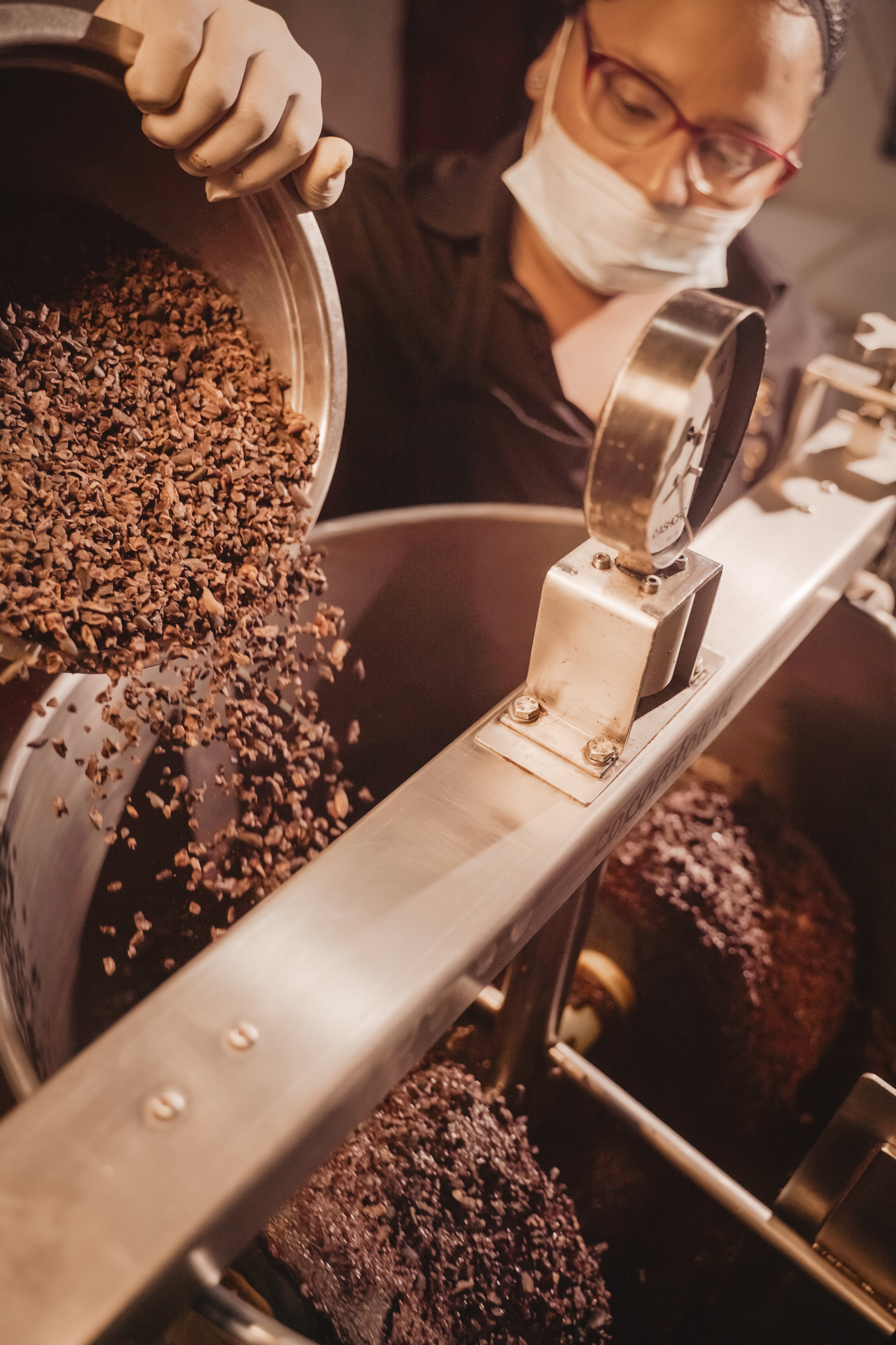 A chocolate maker pouring cacao nibs into the stone melangeur at Oro&