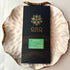Oro Ginger 78% cacao bar in black packaging on a gold-rimmed white porcelain plate, seen from above