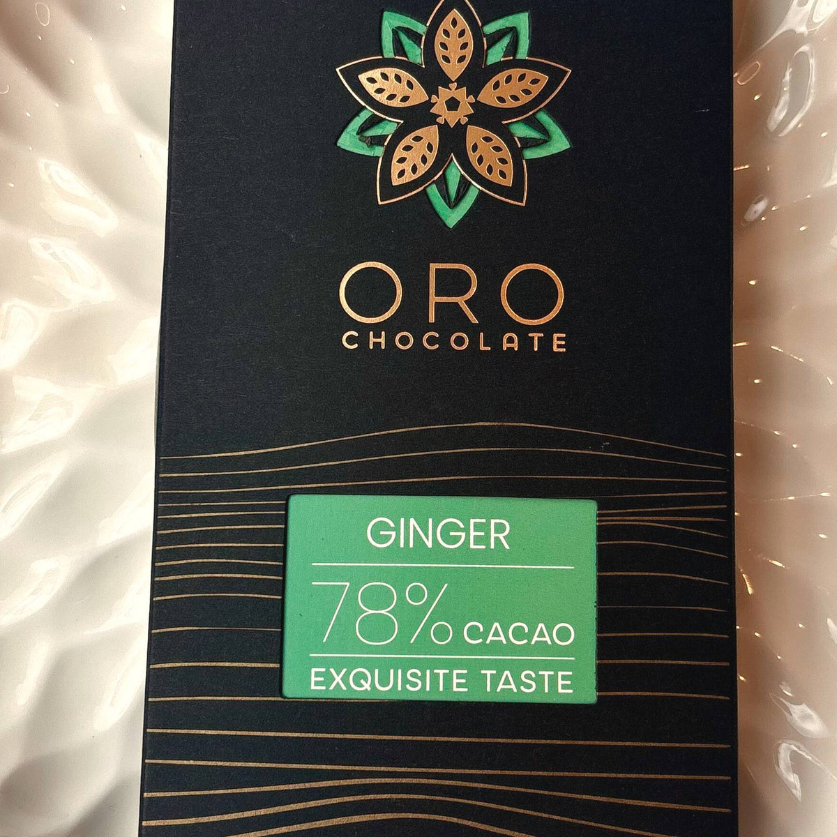 Close-up of the Oro Ginger 78% cacao chocolate bar label and the gold Oro flower mark on the black pack