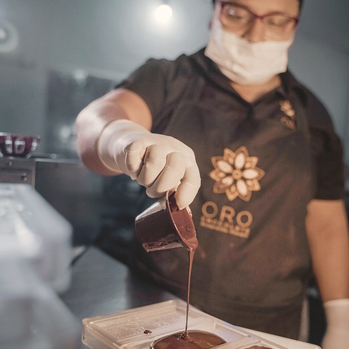 Tempered chocolate being poured by hand from a jug into a bar mold