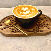 A latte with a leaf poured in the foam, on a wooden tray scattered with roasted coffee beans