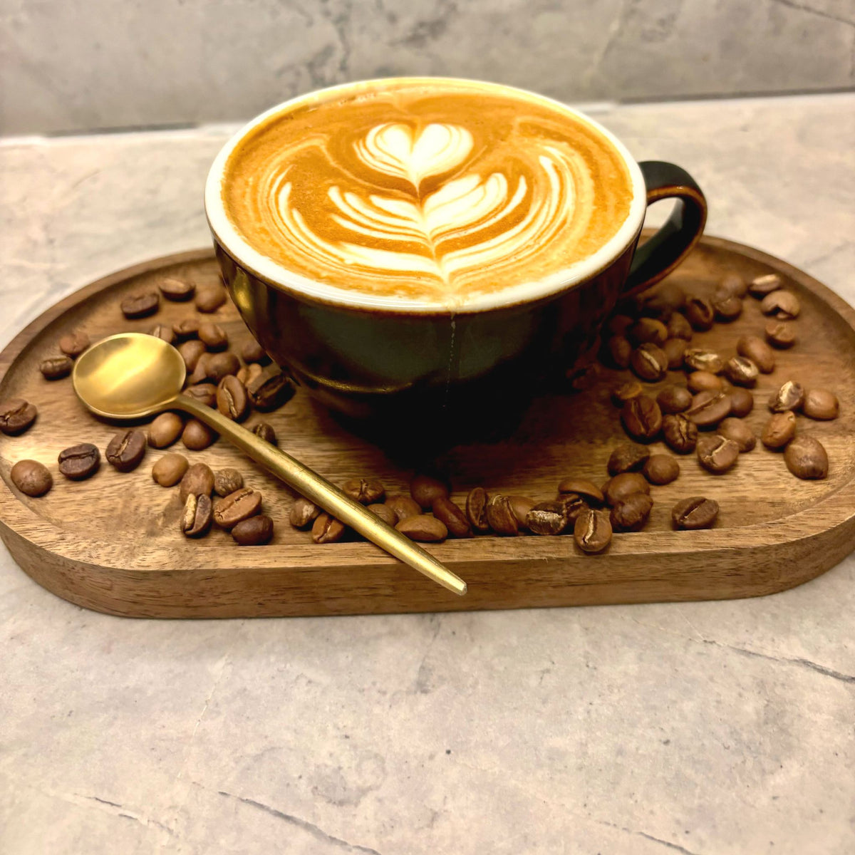 A latte with a leaf poured in the foam, on a wooden tray scattered with roasted coffee beans