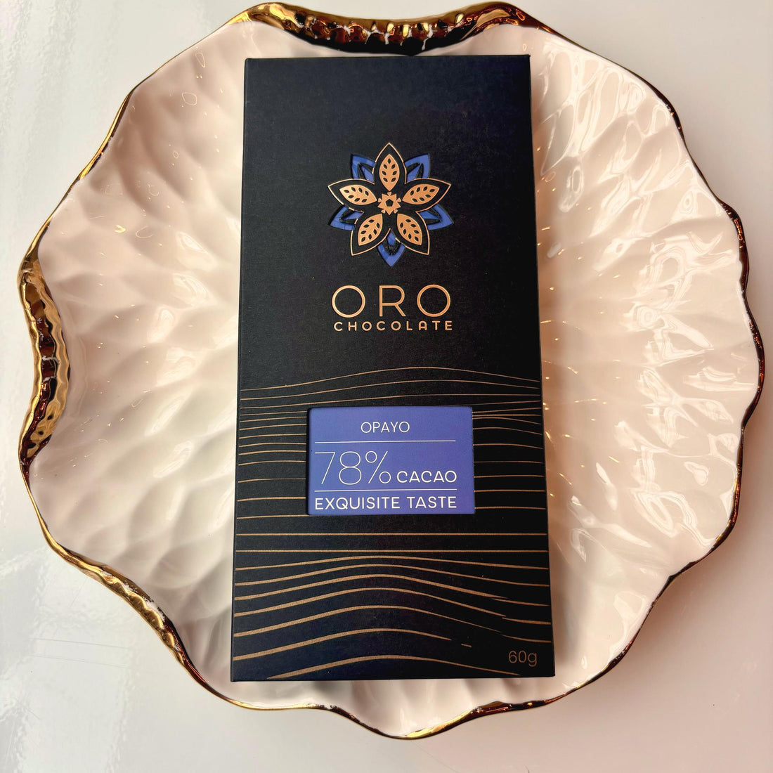 Oro Opayo 78% cacao bar in black packaging on a gold-rimmed white porcelain plate, seen from above