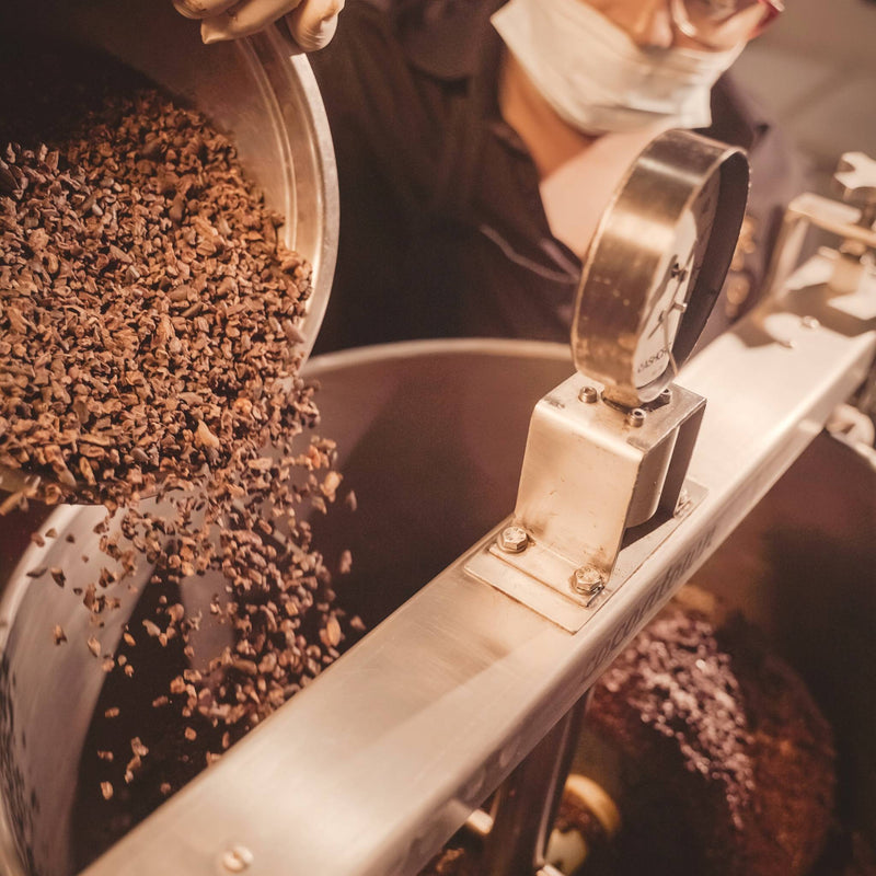 A chocolate maker pouring cacao nibs into the stone melangeur at Oro's Wicker Park factory