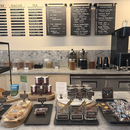 Pastries, bark and chocolate on trays at the counter at Oro, the drink boards on the wall above