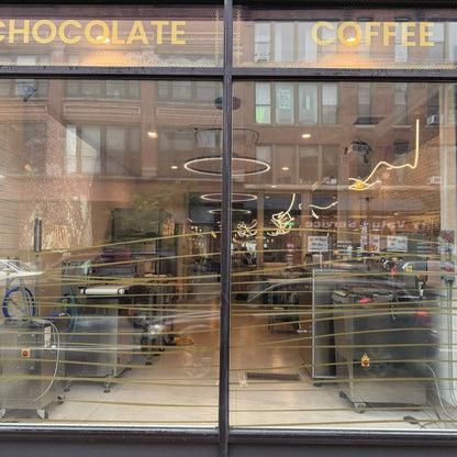 The front window of Oro on Milwaukee Avenue, gold letters reading Chocolate and Coffee, the chocolate equipment behind the glass