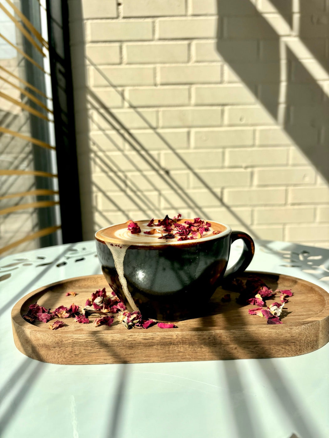 A rose latte with dried petals on a wooden tray, in morning sun at the Oro cafe