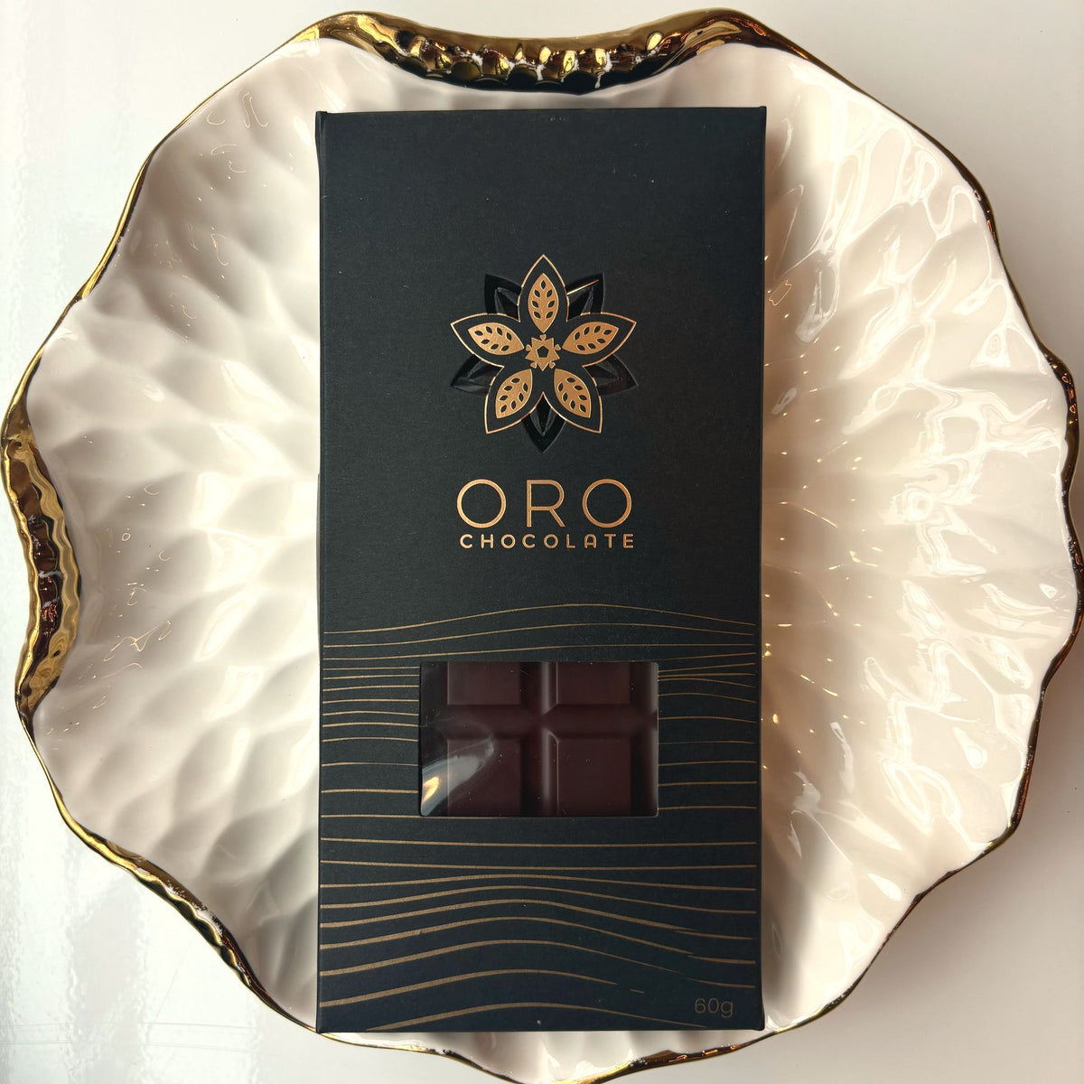 Oro Sea Salt 78% cacao bar in black windowed packaging on a gold-rimmed white porcelain plate, seen from above