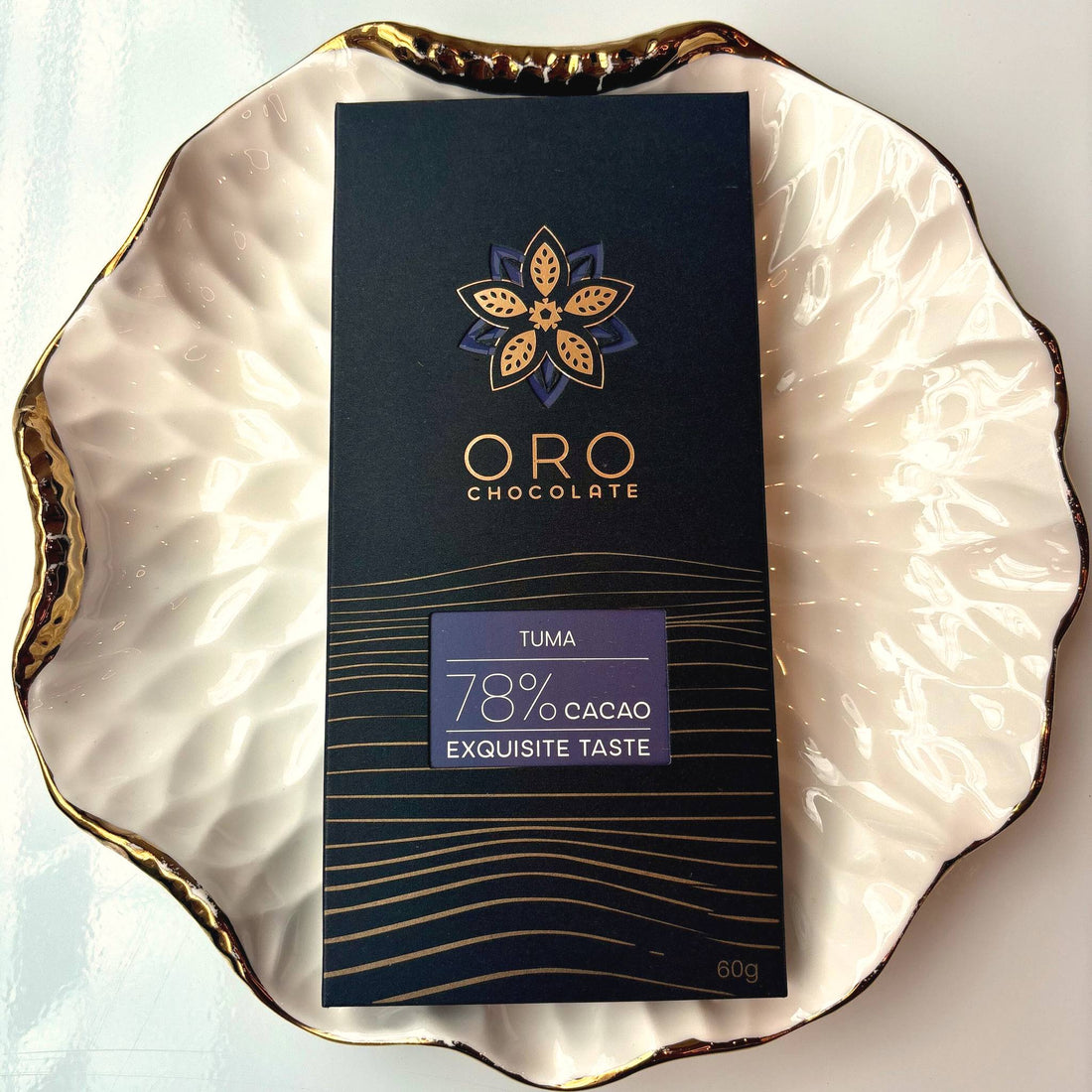 Oro Tuma 78% cacao bar in black packaging on a gold-rimmed white porcelain plate, seen from above
