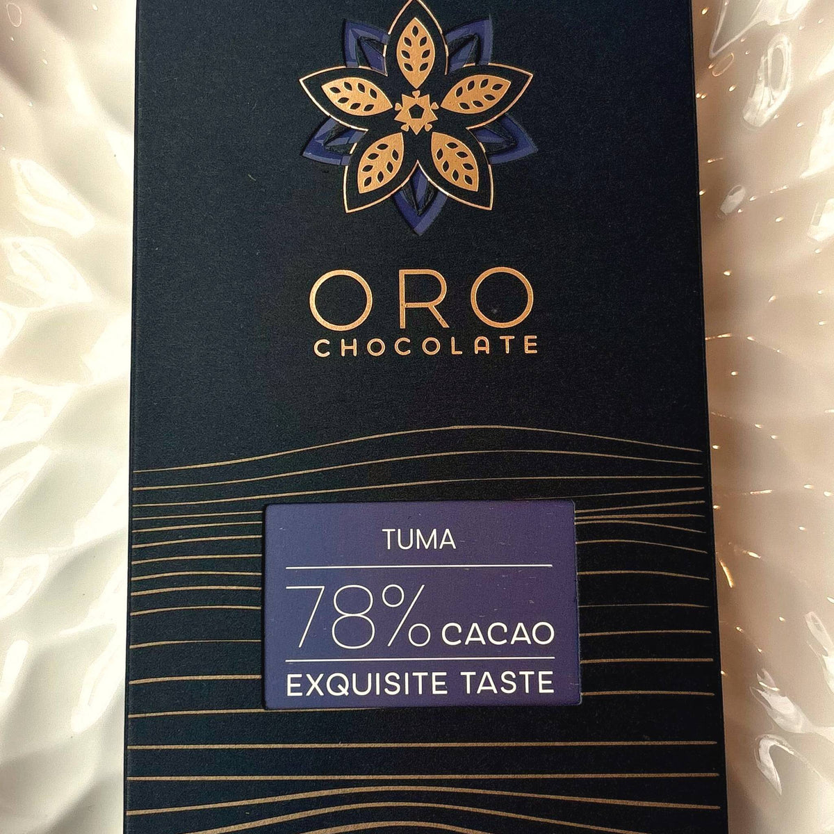 Close-up of the Oro Tuma 78% cacao chocolate bar label and the gold Oro flower mark on the black pack